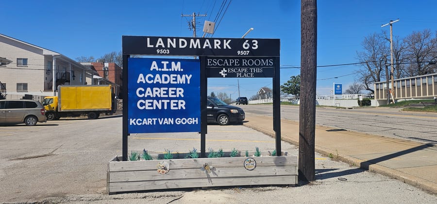 The Landmark 63 sign on East 63rd Street: a blue panel reading A.I.M. Academy Career Center and KC Art Van Gogh at 9503, beside a panel for escape rooms at 9507.